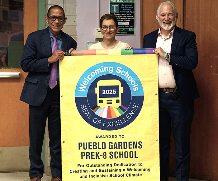 Three people smile while holding a Welcoming Schools Seal of Excellence banner