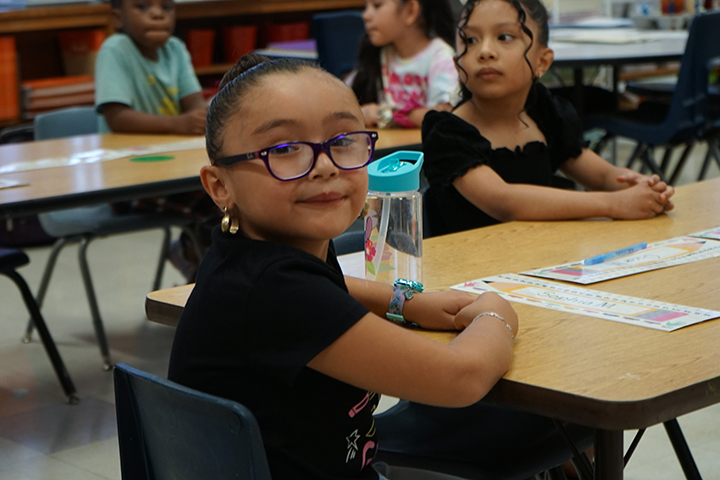 A little girl in glasses turns around and smiles