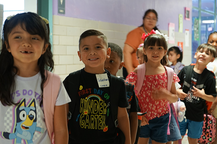 A group of students smile in the hallway as they line up to go into the classroom