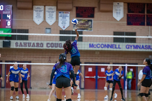 A girl jumps up to spike the volleyball over the net