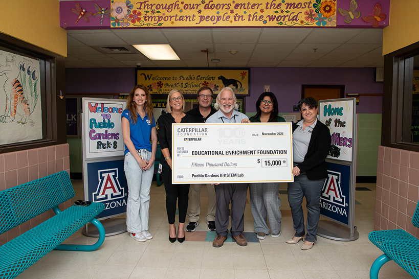 A group of people smile while holding a giant check in the school hallway