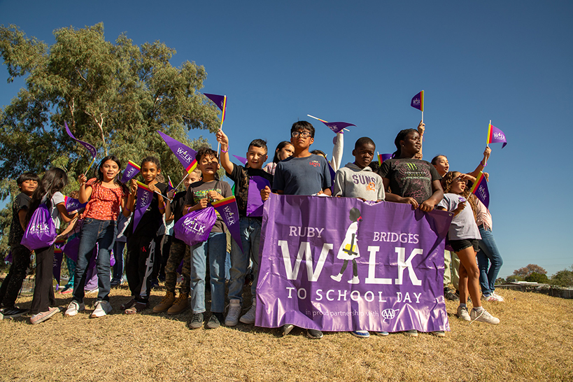 Students hold up a purple Ruby Bridges Walk to School Day banner and pennants
